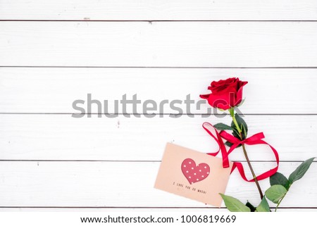 Valentine's day congratulation. Red rose and greeting card with heart sign on white wooden background top view copy space
