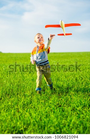 Happy kid playing with toy airplane against blue summer sky background.  Boy throw foam plane in green field. Best childhood concept.