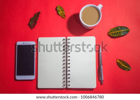 Minimalist workspace on top view with copy space. A cup of coffee, blank notebook, smartphone ,silver pen on red background