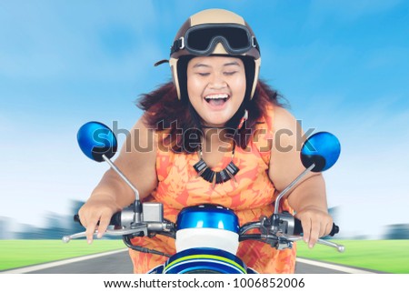 Picture of happy obese woman closing her eyes while riding a scooter on the highway