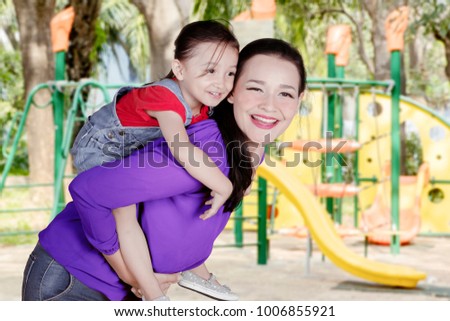 Picture of Caucasian woman looks happy while giving a piggyback ride her daughter in the playground