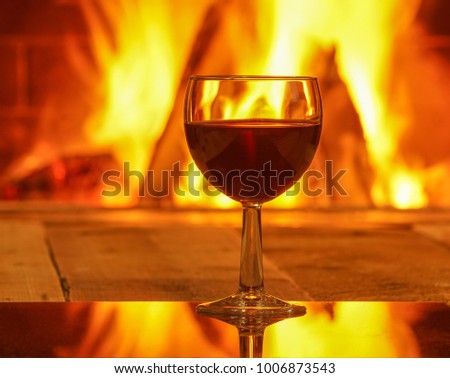 Glass of red wine before cozy fireplace background, winter vacation, 