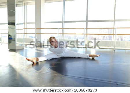 Male person doing physical exercises at gym studio. Young person training in white shirt and pants. Concept of making arms stronger, athletic and dance school. 