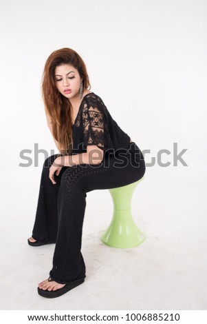 Young pretty girl in black dress sitting on green chair on white background