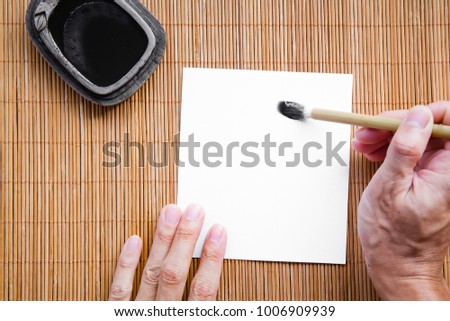 Abstract man hand hold calligraphy brush with white paper and and inkstone on bamboo   mat. picture for add text or greeting card chinese new year. Chinese traditional painting text