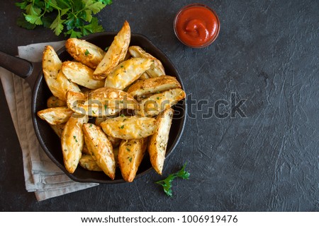 Baked potato wedges with cheese and herbs and tomato sauce on black background - homemade organic vegetable vegan vegetarian potato wedges snack food meal. Royalty-Free Stock Photo #1006919476