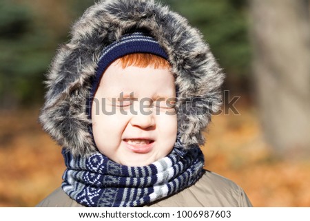picture of a young child during a walk in the park in the autumn season. the boy squinted against the sunlight
