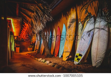 A collection of different colorful surf boards used as a decoration next to a walkway, resting on a wall. Photo taken during the night with a bunch of surfboards on the sand. Surfboards at night