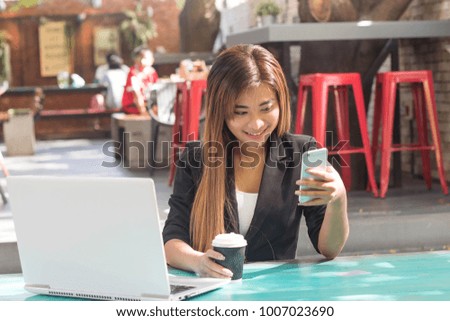 Young business women using smartphone and laptop at outdoor coffee shop.