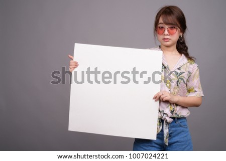 Studio shot of young beautiful Asian tourist woman wearing Hawaiian shirt ready for vacation against gray background