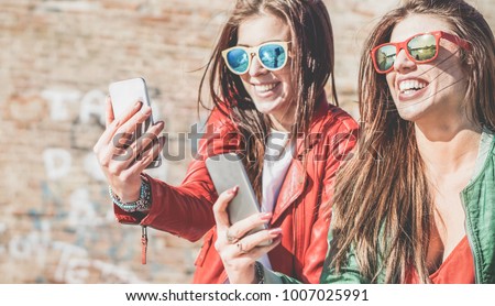 Happy fashion friends watching videos on smartphone - Girlfriends having fun social technology trends outdoors - Friendship, youth lifestyle, millennials generation and tech concept Royalty-Free Stock Photo #1007025991