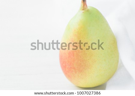 Single Ripe Organic Pear in Pastel Green Yellow Red Colors Linen Fabric on White Wood Background. Elegant Minimalist Japanese Style. Creative Image for Social Media Blog Product Branding. Copy Space