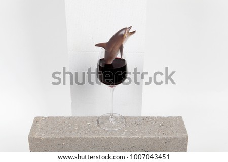 a dolphin plastic toy inside a glass of red wine. Minimal funny and quirky design still life photography