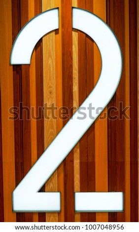 Large 2 with natural wood paneling background. Stencil style white number 2 with polished wood paneling in background behind it.