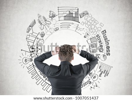 Portrait of a blond businessman wearing a suit and pulling out his hair in panic. A rear view. A concrete wall with a round business plan sketch.