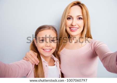 Smiling, nice, sweet, cute mother and daughter with beaming smiles, making selfie together on smart phone, front camera over gray background Royalty-Free Stock Photo #1007060797