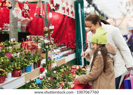 Happy woman with little daughter looking at adornment with conifer in Christmas market. Focus on girl