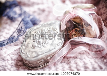 Dried flowers (rose, black viburnum) from a bridal bouquet in a glass jar and silver box with floral pattern on pink knit background.