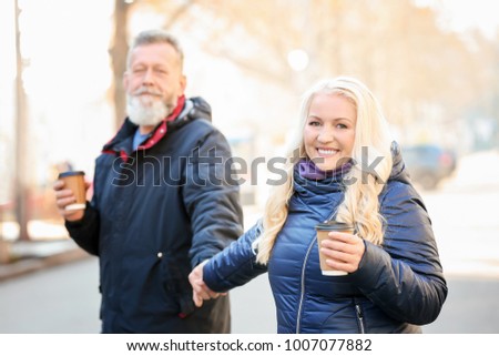 Happy mature couple walking in the street and drinking coffee on autumn day