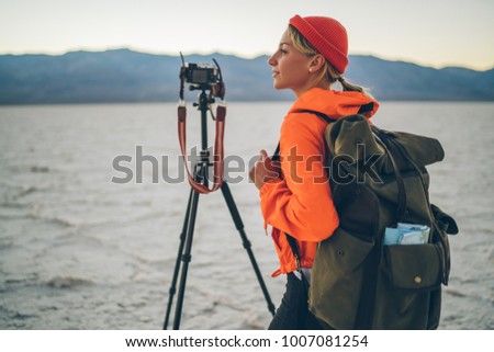Young traveler shooting video on camera having expedition in wild lands of dry lake in Badwater basin,positive female photographer enjoying woks exploring environment of Death valley during sunset