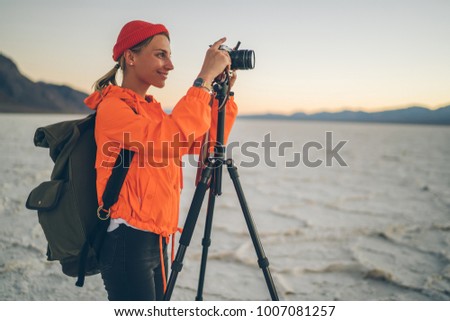 Smiling female photographer making pictures of natural landscape of Badwater basin enjoying travel, woman blogger using tripod and digital camera shooting scenic view of wild area of Death valley