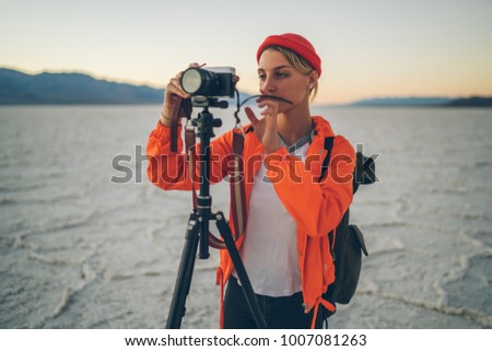 Pensive female journalist concentrated on making setting for shooting view of landscape in expedition, skilled photographer taking pictures of natural landscape in Badwater national park using tripod