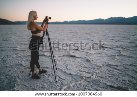 Young female photographer shoot sunset in Death Valley using digital camera and tripod, tourist woman making pictures of wild landscape of Badwater basin in evening dusk having journalistic expedition