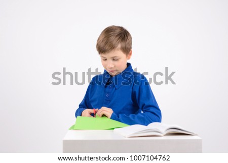 origami: studious boy with scissors is studying the book to make crafts out of paper