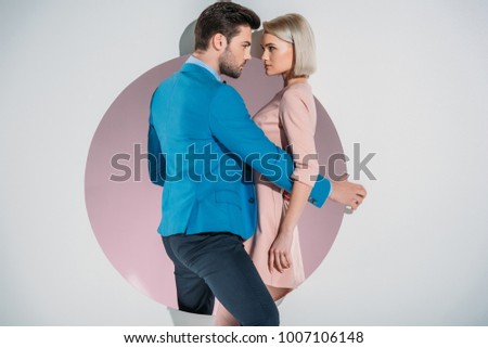 beautiful stylish young couple looking at each other while standing on hole on grey