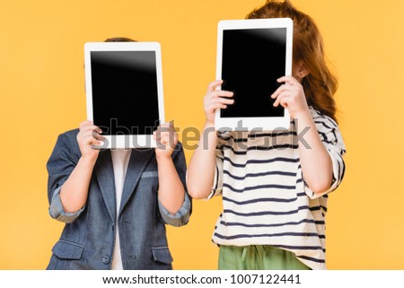 obscured view of kids holding tablets with blank screens isolated on yellow