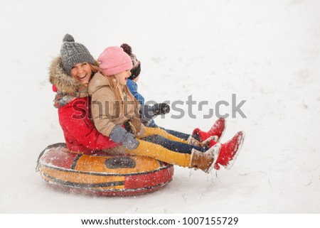 Image of mother with her daughter and son riding tubing in snowfall