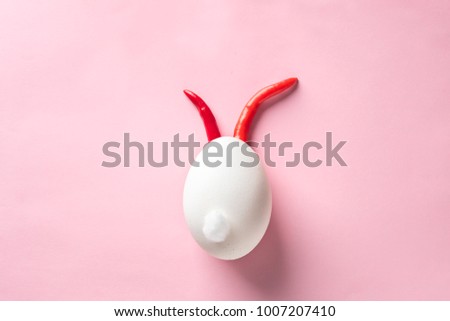 Egg shell and red hot chilli pepper imitation rabbit, hare face of devil clown on pink colored background paper. Food concept minimal Easter Halloween