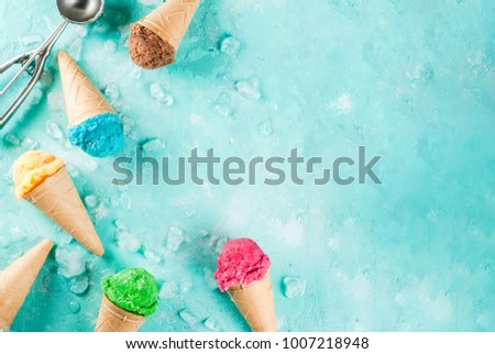 Selection of various bright multicolored ice-cream in ice cream cones - chocolate vanilla blueberry strawberry pistachio orange, on light blue sunny background, copy space top view