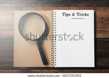 magnifying glass and notebook with TIPS AND TRICKS word with copy space on wooden table. tips and tricks concept