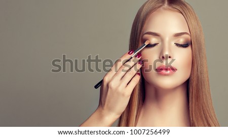  Makeup artist applies  eyeshadow  . Beautiful woman face. Hand of make-up master, painting eyes of young beauty  model girl . Make up in process