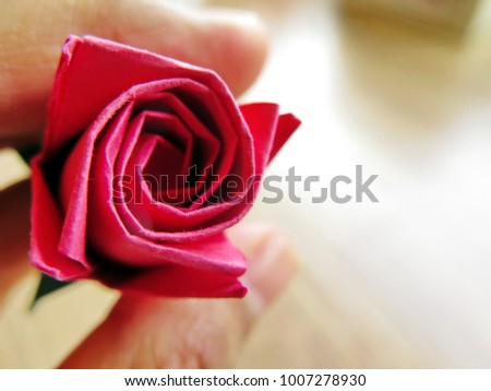Origami flower in blurry holding fingers on wood background, red rose paper for Valentine's day concept, have copy space