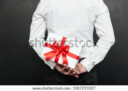 Cropped image from back of man holding white present box with red bow in hands isolated over dark gray wall