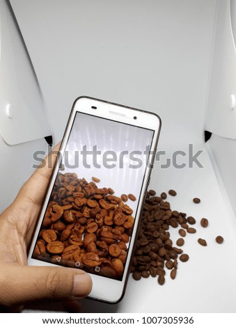 studio shooting of coffee beans with smartphone, white background, human hand 
