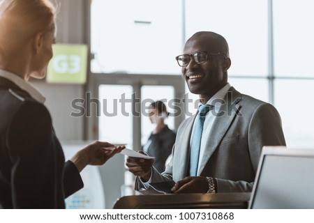 happy young businessman giving passport and ticket to staff at airport check in counter Royalty-Free Stock Photo #1007310868