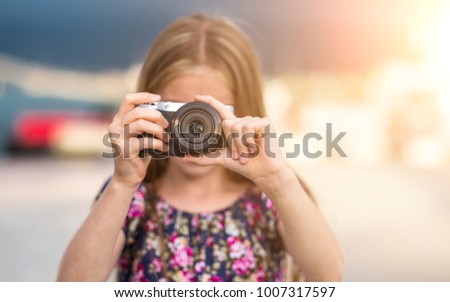 Beautiful little girl with camera takes a picture, summer outdoor