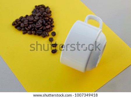 Coffee beans in shape of heart  with white cup on yellow background. valentines concept.