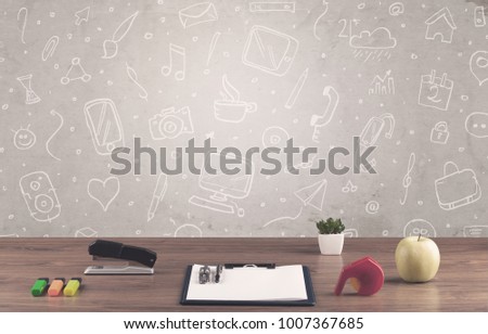 Close up of business office desk with laptop tablet in front of brown wall background full of drawn communication icons and school items concept
