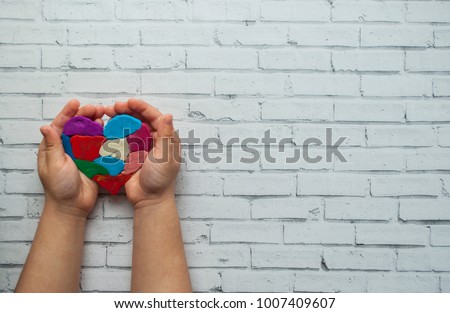 Child's hands holding a multicolored heart on white background with place for your text. World autism awareness day concept. Royalty-Free Stock Photo #1007409607