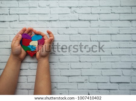 Child's hands holding a multicolored heart on white background with text space. World autism awareness day.