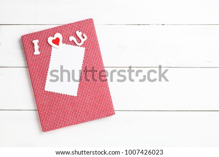 Red cloth frame or notebook with the letter I, heart, U that reads I Love You and paper for text input. All placed on beautiful rustic white wood planks. The concept of Valentines Day. Copy space