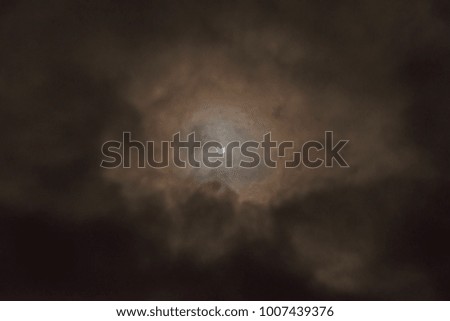 The moon and sun in a partial eclipse with ominous clouds surrounding them