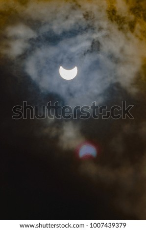 The moon and sun in a partial eclipse with ominous clouds surrounding them