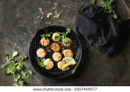 Fried scallops with butter lemon spicy sauce in cast-iron pan served with green salad and textile napkin over old dark metal background. Top view, space Royalty-Free Stock Photo #1007444077