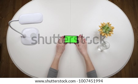 Woman freelancer takes a smartphone and typing using app. Chroma key Green screen. Top view. Hands close up view