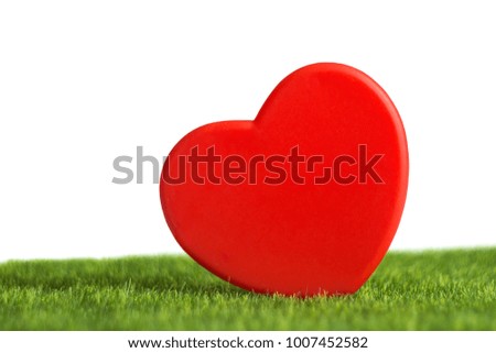 Red plastic heart on artificial grass and white background, studio, close up